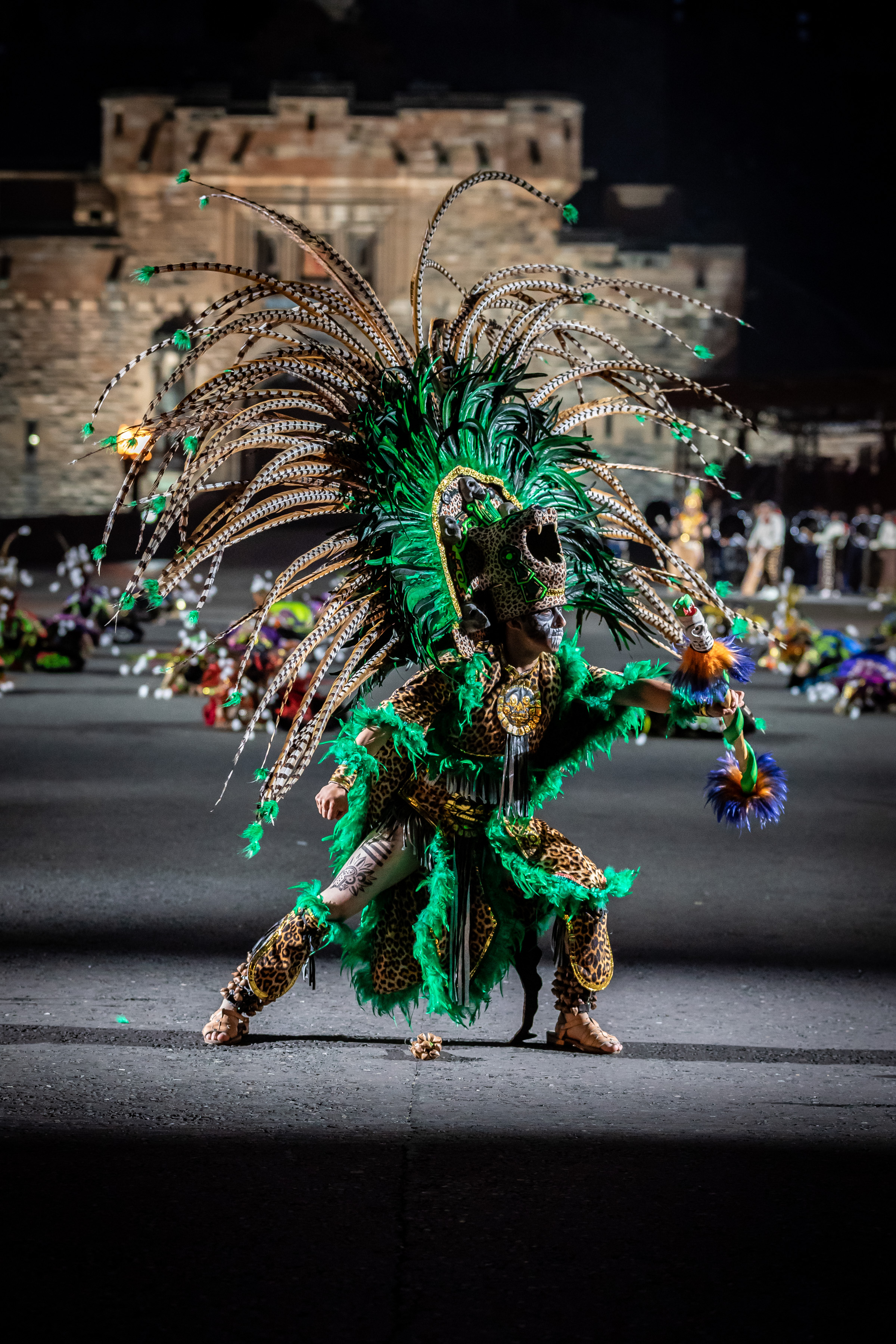 Image shows a Mexican performer wearing green feathers costume and a cheetah head dress.